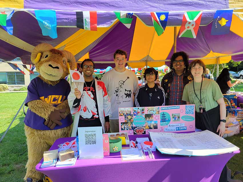 Students and staff standing under an event tent with Rammy.