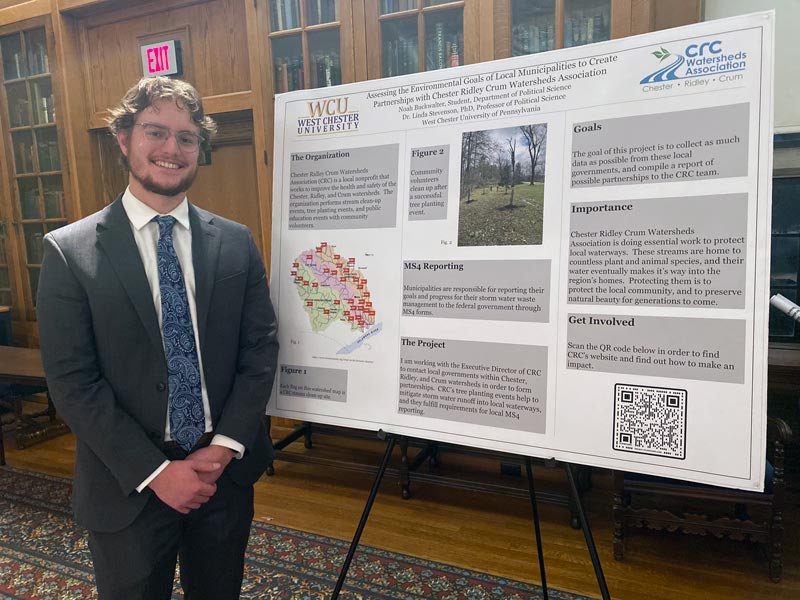 Student standing next to poster board. Text from the poster board follows: West Chester University. Assessing the Environmental Goals of Local Municipalities to Create Partnerships with Chester Ridley Crum Watersheds Association Noah Buckwalter, Student, Department of Political Science Dr. Linda Stevenson, PhD, Professor of Political Science West Chester University of Pennsylvania. CRC Watersheds Association. Chester, Ridley, Crum. The Organization. Chester Ridley Crum Watersheds Association (CRC) is a local nonprofit that works to improve the health and safety of the Chester, Ridley, and Crum watersheds. The organization performs stream clean-up events, tree planting events, and public education events with community volunteers. Figure 1, CHESTER CREEK WATERSHED Showing approximately 25 flags, each flag on this watershed map is a CRC stream clean-up site. Figure 2, community volunteers clean up after a successful tree planting event. MS4 Reporting. Municipalities are responsible for reporting their goals and progress for their storm water waste management to the federal government through MS4 forms. The Project. I am working with the Executive Director of CRC to contact local governments within Chester, Ridley, and Crum watersheds in order to form partnerships. CRC's tree planting events help to mitigate storm water runoff into local waterways, and they fulfill requirements for local MS4 reporting. The goal of this project is to collect as much data as possible from these local governments, and compile a report of possible partnerships to the CRC team. Importance. Chester Ridley Crum Watersheds Association is doing essential work to protect local waterways. These streams are home to countless plant and animal species, and their water eventually makes it's way into the region's homes. Protecting them is to protect the local community, and to preserve natural beauty for generations to come.