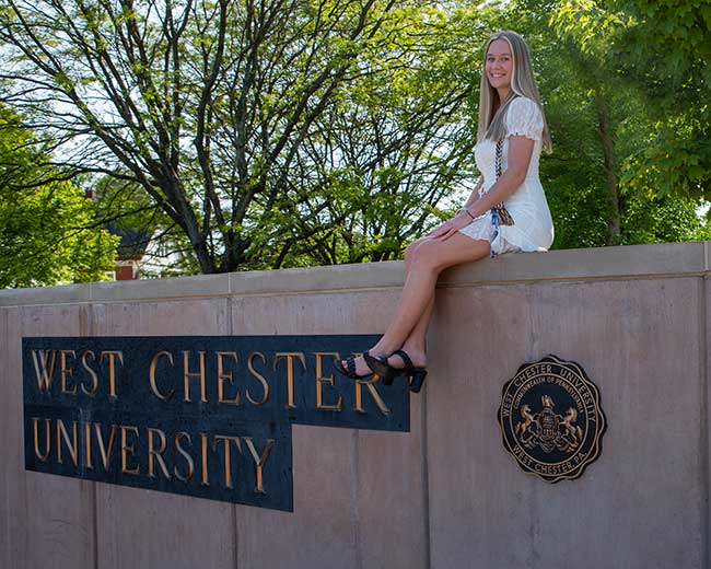 large, student sitting on wall, sign West Chester University