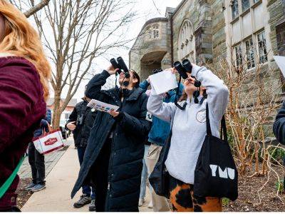 Two students using binoculars look up, trying to spot birds.