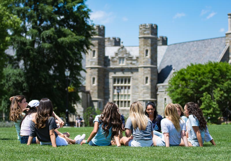 A circle of students sitting in the academic quad with Phillips building in the background