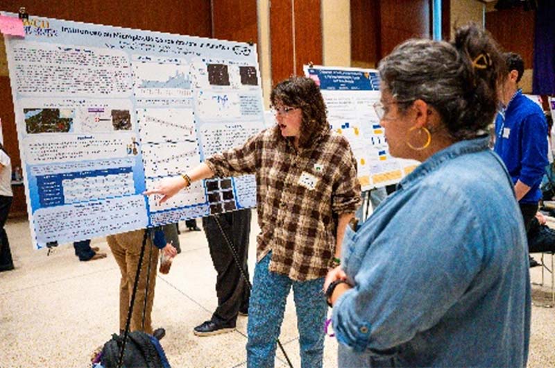 A women stands in front of her posting board and points to a specific spot on the poster