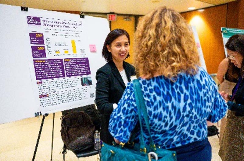 A women stands talking to another woman in front of a poster board