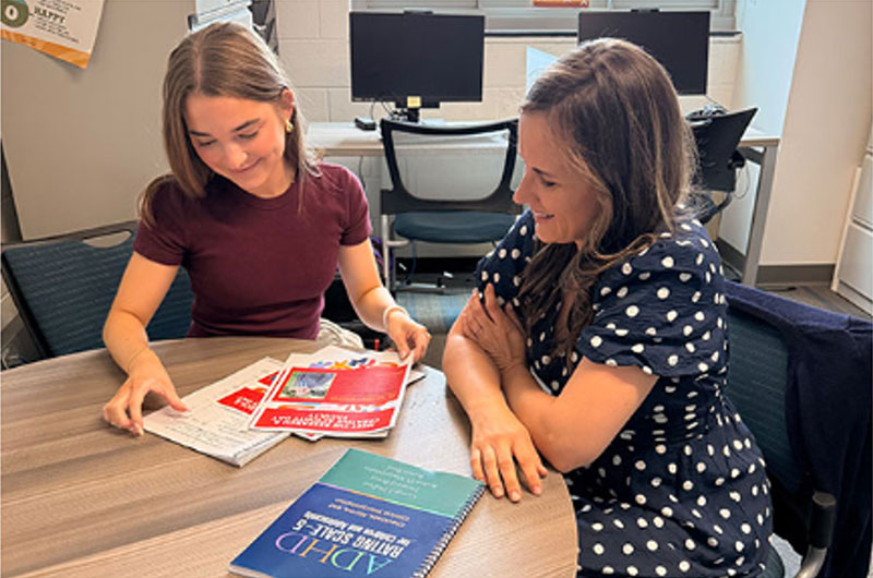 Two women sit at a table looking through brochures