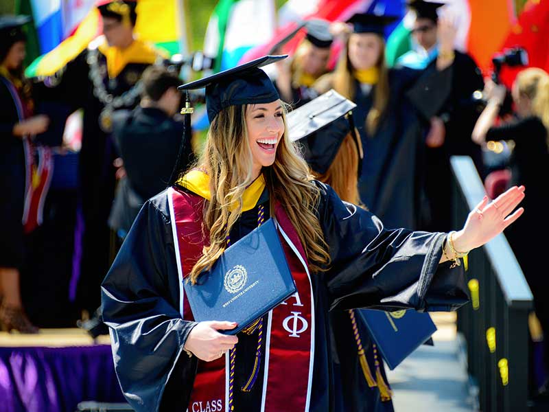 a student at commencement holding her diploma and waving