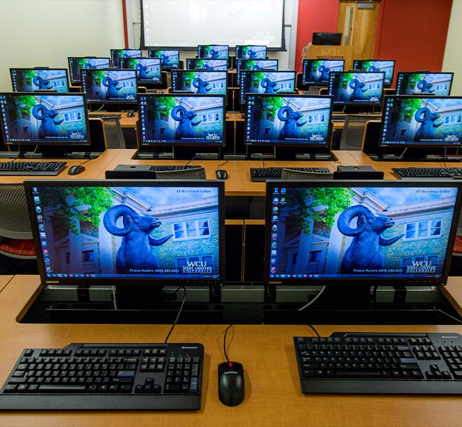 A classroom full of desktop monitors which all have the WCU ram as their backgrounds