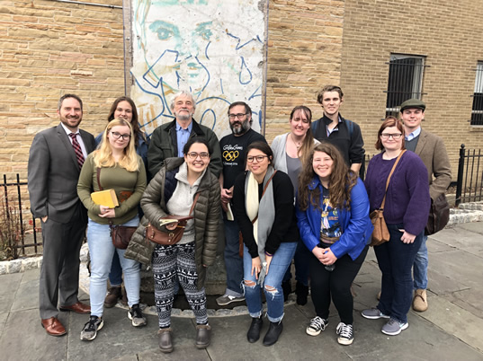 West Chester University student co-curators and faculty advisor Michael A. Di Giovine (back row, left) examine a piece of the Berlin Wall on permanent display at the German Society of Philadelphia, on a study trip hosted by the society’s director, Anton “Tony” Michels (center, back row)