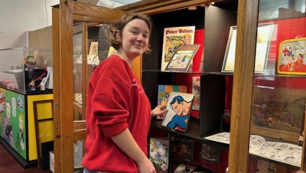 Student co-curator Lilli Benson arranges Superman and other comics artifacts in one of the exhibition cases.