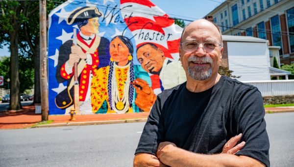 WCU music alumnus Al Moretti ’73, M’82 standing in front of the West Chester250 mural downtoqn