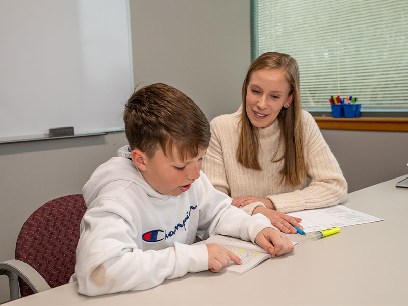 A student teacher sits at a desk and teaches a young student