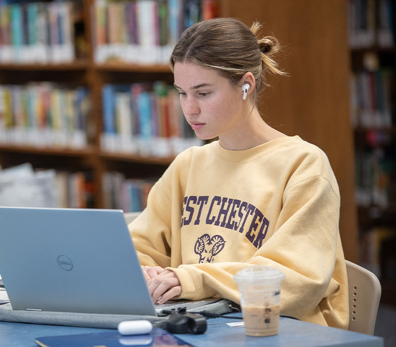 A student wearing a yellow WCU sweatshirt is working on her laptop