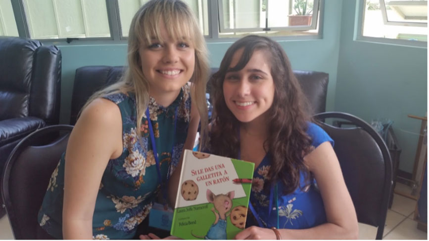 Two women posing holding the book 'If You Give a Mouse a Cookie' [in Spanish].