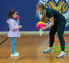 Adult standing with child. Adult is holding a rainbow colored basketball.