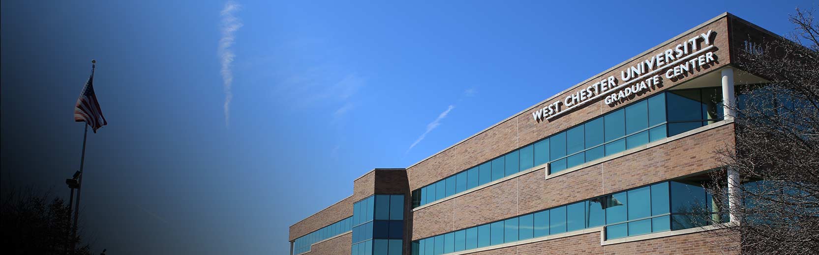 Exterior view of the West Chester University Graduate Center building under a clear blue sky, with an American flag on a pole nearby.