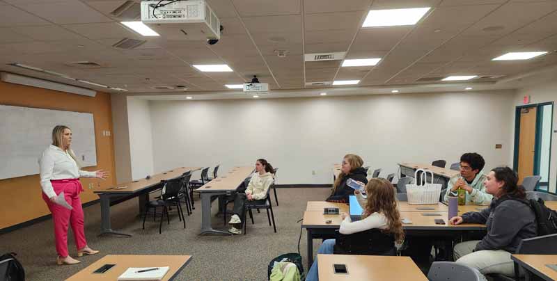 Sarah Fedor stands at the front of a classroom full of people while delivering a talk